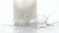 Milk splashing out of glass with dynamic liquid motion and droplets frozen in mid-air, suitable for beverage, dairy, and food photography projects.