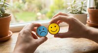 Hands holding colorful emoji faces showing sad and happy emotions for mental health awareness and positive thinking concepts.
