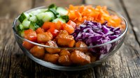 Fresh poke bowl with diced salmon, purple cabbage, cucumber, and carrots served in glass bowl on rustic wooden table, healthy Asian cuisine.