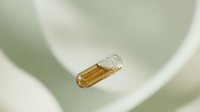 Transparent capsule with golden liquid supplement floating in soft green curved background for health and wellness concepts.