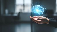 Glowing blue brain hologram floating above open palm in modern office environment representing artificial intelligence and neural network technology.
