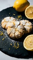 Homemade lemon crinkle cookies dusted with powdered sugar on dark slate board with fresh citrus slices and zest for baking and dessert recipes.