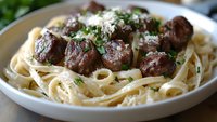 Juicy beef meatballs served on creamy fettuccine pasta with grated parmesan cheese and fresh herbs garnish in white plate.