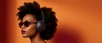 Young African American woman with afro hair wearing headphones and sunglasses against vibrant orange background, music and lifestyle concept.