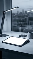 Modern office workspace with LED desk lamp, tablet, wireless charger and coffee cup on white desk near window overlooking city skyline for productivity concepts.