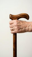 Elderly hand with wedding ring gripping a wooden walking cane on light background, symbolizing aging, mobility aid, and senior independence.