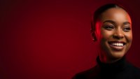 Happy African American woman smiling warmly against red background wearing black turtleneck for lifestyle and portrait photography projects.