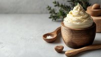Creamy whipped butter in rustic wooden bowl with spoons on light textured background, fresh herbs and natural ingredients for cooking and baking.
