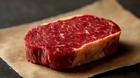 Raw ribeye steak with marbled fat on butcher paper ready for grilling, premium beef cut for cooking and culinary preparation.