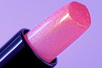 Shimmering pink lipstick bullet with sparkly glitter finish against purple background, macro cosmetic photography showing luxurious texture and shine.