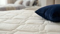 Cream quilted mattress with navy blue pillow on bed, showcasing comfortable bedding for bedroom interior design and home decor projects.