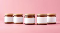 Small glass jars with wooden lids arranged in row on pink background, blank white labels for mockup, minimalist product presentation for cosmetics or food.