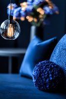 Glowing vintage Edison bulb pendant lamp illuminates cozy blue interior with decorative sphere and soft cushions, creating moody evening atmosphere.