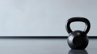 Single black kettlebell on wooden floor against white wall in minimalist gym setting for fitness and strength training workouts.