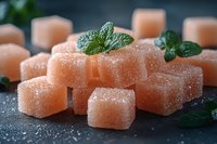 Orange fruit jelly cubes with sugar coating and fresh mint leaves on dark slate surface for confectionery and dessert concepts.
