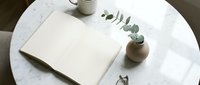 Open blank notebook on marble table with eucalyptus in vase, coffee cup and glasses, minimal Scandinavian home decor flat lay.