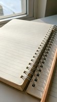 Open spiral notebook with blank lined pages on wooden desk near window for writing, journaling, note-taking, planning, and creative work in natural light.
