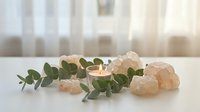 Spa wellness setup with burning candle, eucalyptus branch and himalayan salt crystals on white table creating peaceful relaxation atmosphere for meditation.