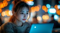 Young Asian woman working on laptop at night with colorful bokeh lights in background, creating atmospheric mood for remote work and digital lifestyle.
