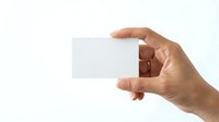 Close-up of a hand holding a blank white business card or paper against a neutral background for branding and corporate identity mockups.