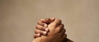 Two hands clasped together in prayer or meditation pose against warm beige background, symbolizing unity, faith, spirituality and human connection.
