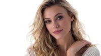 Young blonde woman with natural makeup and wavy hair wearing beige sweater smiling at camera against light background, beauty and fashion portrait.