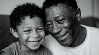 Father and young son, both African descent, smiling together on couch in black and white portrait. Genuine family bonding moment capturing love and joy between generations for parenting, family relationships.