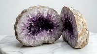 Split amethyst geode displaying deep purple crystal formations with natural rock exterior on marble surface for mineral collection and healing practices.