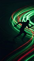 Dynamic runner silhouette with vibrant green and red light trails creating motion blur effect on dark background for sports and fitness concepts.