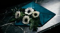 White anemone flowers with dark centers arranged on teal envelope against marble surface for elegant correspondence and floral design projects.