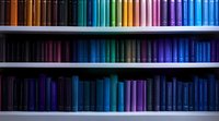 Colorful book spines arranged in rainbow spectrum order on library shelves, transitioning from dark to vibrant hues, creating visual gradient pattern.