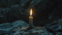 Single burning white candle glowing in darkness on rocky surface against moody teal background, creating atmospheric spiritual ambiance.