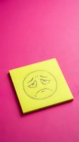 Yellow sticky note with hand-drawn sad face emoji on vibrant pink background for mental health awareness and emotional expression concepts.