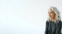 Mature woman with long gray hair wearing dark gray sweater, looking away thoughtfully against white background. Suitable for lifestyle, wellness, and aging gracefully concepts.