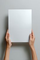 Female hands holding blank white paper sheet against gray background, mockup for presentation, branding, and design projects.