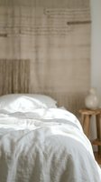 Unmade bed with white linen sheets and pillows in minimalist bedroom interior with wooden nightstand and neutral wall decor for home design projects.