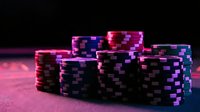 Colorful casino poker chips stacked on gaming table with dramatic neon lighting creating vibrant purple and pink atmosphere for gambling entertainment.
