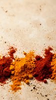 Spice powders including turmeric and paprika scattered on neutral surface with scattered peppercorns, suitable for culinary, food styling and cooking content.