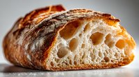 Artisan sourdough bread slice showing airy crumb structure with golden crust, rustic bakery loaf cut revealing holes and texture for food photography.