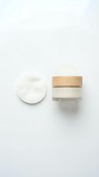 Glass jar of face cream with wooden lid and cotton pad on white background, minimal skincare flat lay for beauty and wellness content.