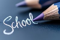 Purple wooden pencil next to handwritten school text on dark background, macro shot with selective focus highlighting education and learning concept.
