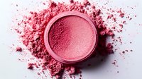Pink crushed makeup powder scattered around circular compact container on white background, creating artistic cosmetic texture and pattern.