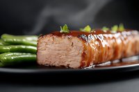 Juicy glazed salmon fillet with bright green asparagus on dark plate, close-up view showing moist flaky texture and caramelized surface garnished with fresh herbs.