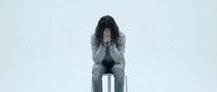 Young woman sitting with head in hands showing depression, anxiety and mental health struggles on white background.