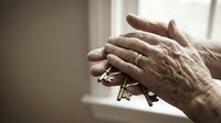 Elderly hands holding vintage keys in soft natural light, symbolizing memories, heritage, and life experiences in warm sepia tones.