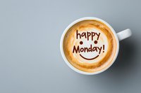Latte art coffee with happy Monday message and smiley face drawn in foam, white ceramic cup on gray background. Positive start of work week concept.
