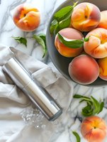Fresh ripe peaches in gray ceramic bowl with green leaves on white textile background, stainless steel water bottle with ice cubes, top view composition.