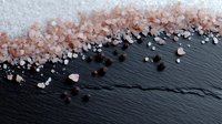 Pink Himalayan salt crystals scattered on black slate stone surface creating diagonal composition with natural texture and contrast for culinary background.