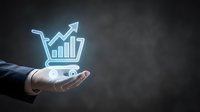 Businessman hand presenting glowing shopping cart with growth chart and upward arrow showing e-commerce sales increase and digital marketing success.