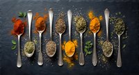 Colorful spices and herbs arranged in vintage metal spoons on dark slate background. Culinary ingredients for cooking and seasoning food preparation.